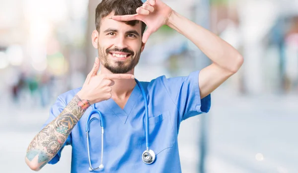 Young handsome nurse man wearing surgeon uniform over isolated background smiling making frame with hands and fingers with happy face. Creativity and photography concept.