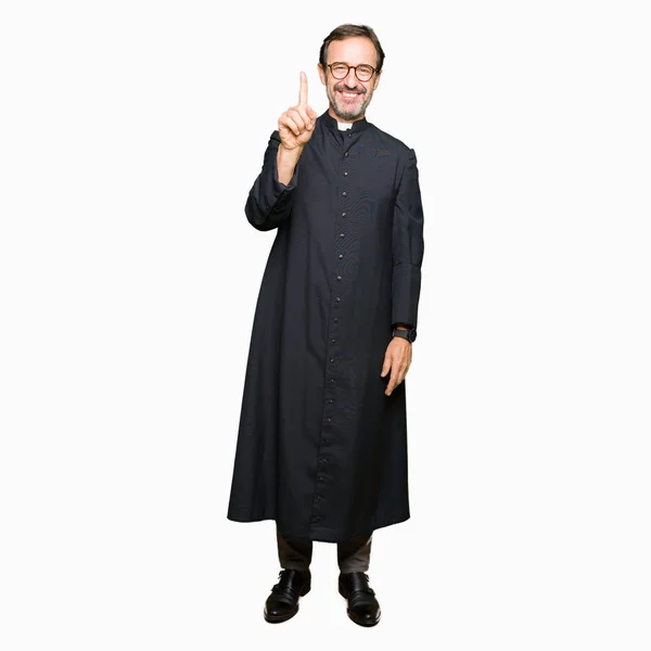 中年牧师男子穿着天主教长袍显示和手指第一 而微笑着自信和快乐 — 图库照片