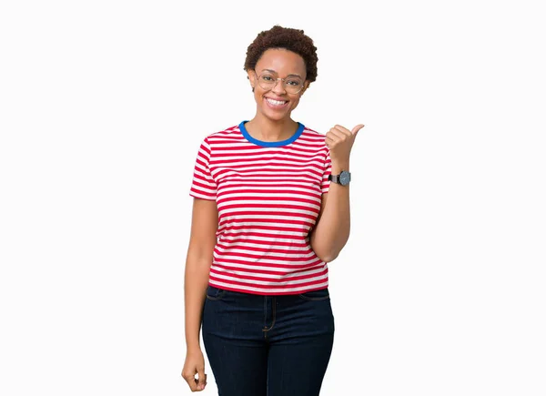 美丽的年轻非洲裔美国妇女戴眼镜在孤立的背景微笑着与快乐的脸看 用拇指指着一边 — 图库照片