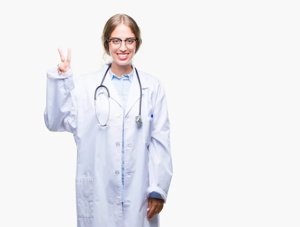 美丽的年轻金发碧眼的医生妇女穿着医疗制服在孤立的背景显示和手指第二 而微笑着自信和快乐 — 图库照片
