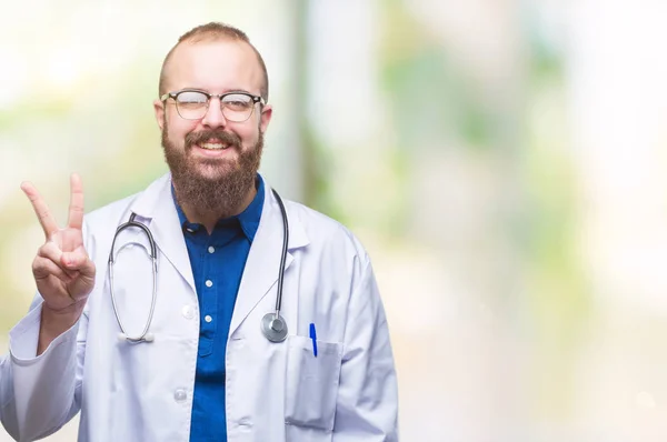 年轻的高加索医生男子穿着医疗白色外套在孤立的背景显示和指向与手指第二 同时微笑着自信和快乐 — 图库照片