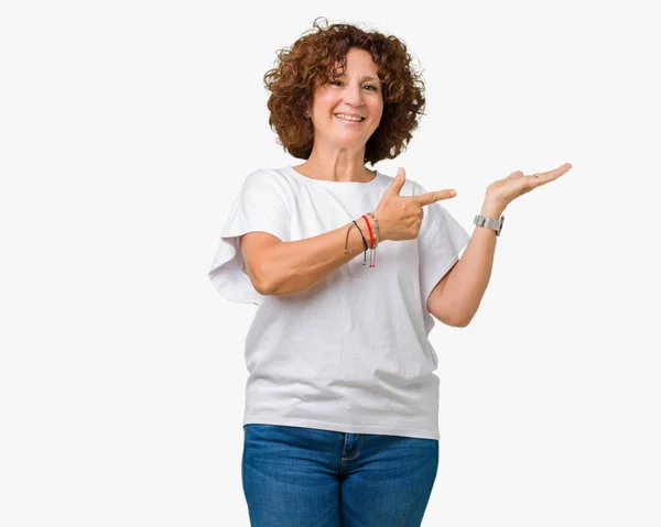 美しい中間エイガー年配の女性を驚かせ カメラにニコニコと手とを提示 指で指している分離の背景に白い シャツを着て — ストック写真