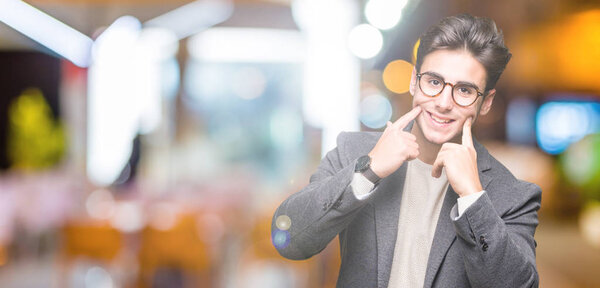 Young business man wearing glasses over isolated background Smiling with open mouth, fingers pointing and forcing cheerful smile