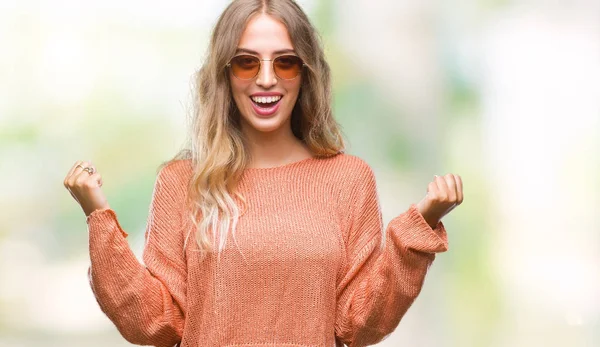 Sarışın kadın izole arka plan kutlama üzerinde güneş gözlüğü takıyor şaşırttı ve silah ile başarı için hayran güzel genç kaldırdı ve gözleri açık. Kazanan kavramı.