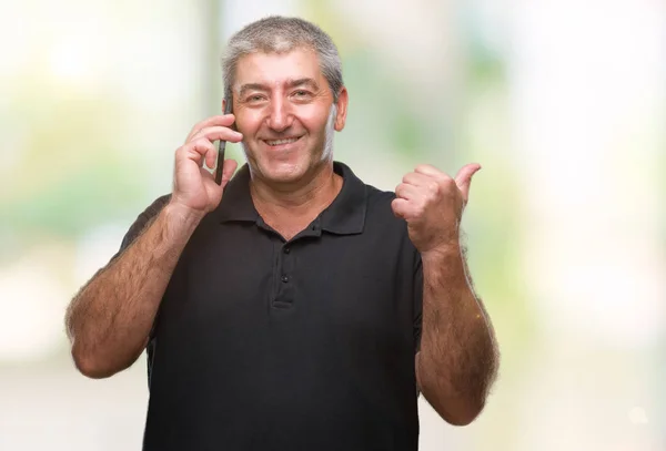 Handsome senior man talking on smartphone over isolated background pointing and showing with thumb up to the side with happy face smiling