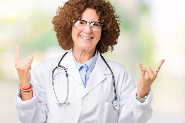 Middle ager senior doctor woman over isolated background shouting with crazy expression doing rock symbol with hands up. Music star. Heavy concept.