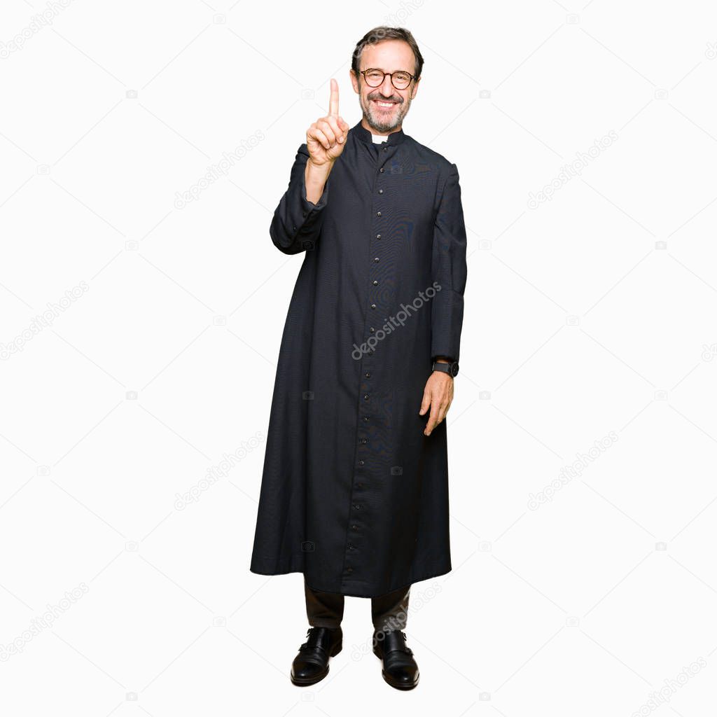 Middle age priest man wearing catholic robe showing and pointing up with finger number one while smiling confident and happy.