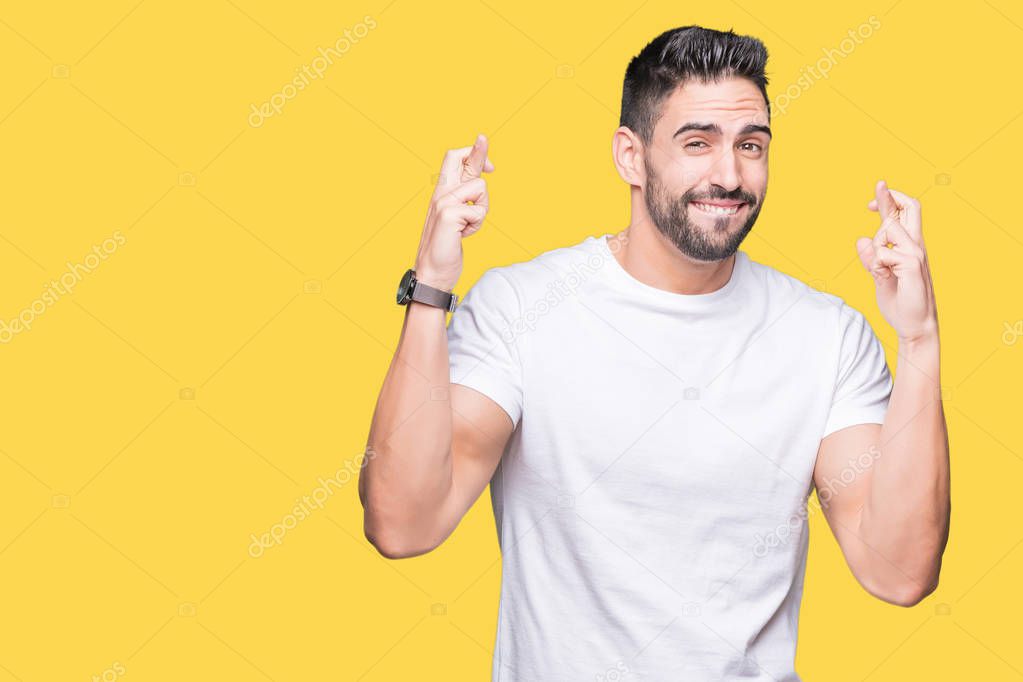 Young man wearing casual white t-shirt over isolated background smiling crossing fingers with hope and eyes closed. Luck and superstitious concept.