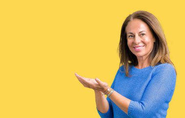 Orta yaş üzerinde kış kazak giyen güzel kadın izole arka plan el ve reklam mutlu ve kendinden emin gülümseyen sunulması avuç, yanında işaret