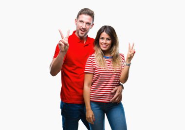 Mutlu yüz zafer işareti yaparken kameraya göz kırpıyor ile gülümseyen izole arka plan üzerinde aşık genç bir çift. İki numaralı.