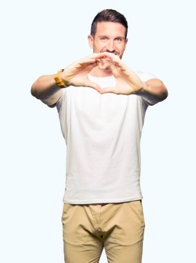 Casual beyaz t-shirt aşık kalp simgesi ve elleriyle şekil gösteren gülümseyen giyen yakışıklı adam. Romantik kavramı.