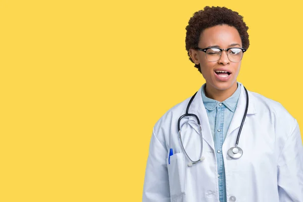 年轻的非洲医生妇女穿着医疗外套在孤立的背景眨眼看着相机与性感的表情 欢快和快乐的脸 — 图库照片