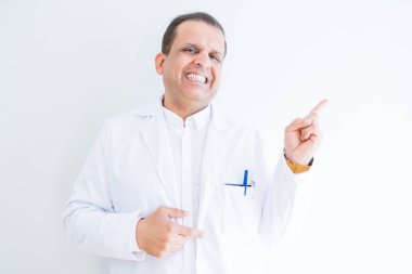 Kameraya bakarak yan el ve parmak ile işaret orta yaş doktor adam yüzünde kocaman bir gülümseme ile beyaz arka plan üzerinde tıbbi bir palto giyiyor.