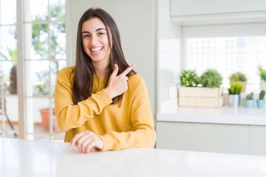 Sarı kazak neşeli bir gülümseme ile el ve parmak kadar yan yüzünde mutlu ve doğal ifade ile işaret yüz giyen güzel genç kadın