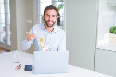 İş adamı yemek götürün Asya erişte yemek çalışma kullanırken bilgisayar dizüstü ve gülümseyen