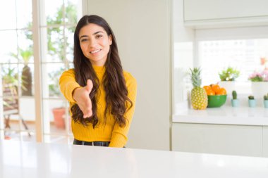 Genç güzel kadın evde dostu sunan el sıkışma tebrik ve davet edici olarak gülümseyen beyaz masada. Başarılı iş.