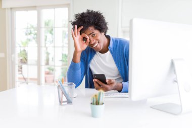 Afrika kökenli Amerikalı adam mutlu yüz el parmaklarının arasından seyir göz üzerinde ok işaretiyle yapıyor gülümseyen ile akıllı telefon ve bilgisayar kullanarak çalışma