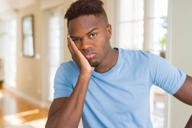 Afro-Amerikan yakışıklı giyiyor rahat t-shirt düşünme seyir yorgun ve sıkılmış çapraz silah depresyon sorunları ile.