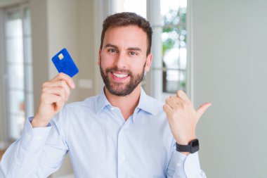 Kredi işaret ve başparmak kadar mutlu yüz gülümseyen tarafı ile gösterilen kartı tutan yakışıklı iş adamı