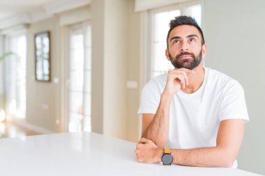 Yakışıklı İspanyol el çene düşünme hakkında soru, dalgın ifade üzerine beyaz tişört evde rahat dostum. Düşünceli yüzüyle gülümsüyor. Şüphe kavramı.