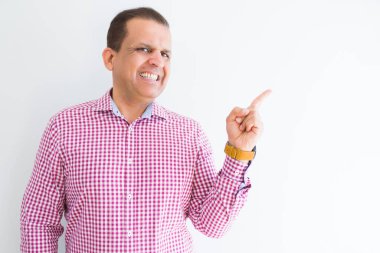 Yüzünde kocaman bir gülümseme ile beyaz duvarın üzerinden iş gömlek giymiş orta yaş adam kameraya bakarak yan el ve parmak ile işaret.