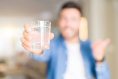 Yakışıklı delikanlı evde bir bardak su içme işaret ve başparmak kadar mutlu yüz gülümseyen tarafı ile gösterilen