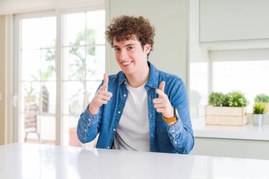 Evde rahat denim ceket giyen genç yakışıklı adam kameraya mutlu ve komik suratla parmakları işaret. İyi enerji ve vibes.