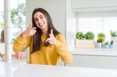 Sarı kazak işaret parmakları için fotoğraf makinesi ile mutlu ve komik yüz giyen güzel genç kadın. İyi enerji ve vibes.