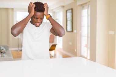 Afro-Amerikan yakışıklı ev umutsuz ve stresli baş ağrısı muzdarip çünkü, beyaz masa üzerinde ağrı ve Migren. Ellerini kafasına.