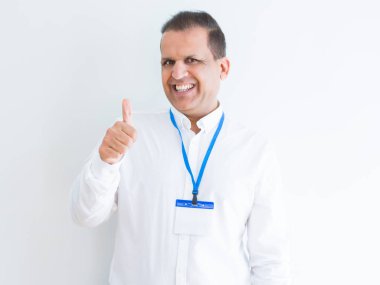 Orta yaş iş adamı mutlu Yaşasın el ile jest yapıyor beyaz arka plan üzerinde kimlik kartı takıyor. Kameraya bakarak başarı gösteren ile ifade onaylama.