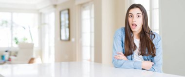 Güzel genç kadın evde korkuyor ve şok sürpriz ifade, korku ve heyecan yüz beyaz masada oturan geniş açı resim.