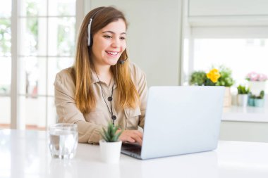Dizüstü bilgisayar ve bir gülen surat konumu olan headseat giyen ve diş gösterilen kendine güvenen bir gülümsemeyle gülümseyerek çalışan güzel genç operatör kadın