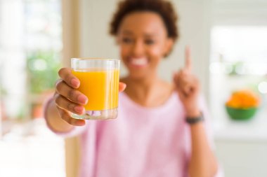 Genç Afrikalı Amerikalı kadın driking portakal suyu evde bir fikirle sürpriz veya işaret parmağı ile mutlu yüz soru, number one