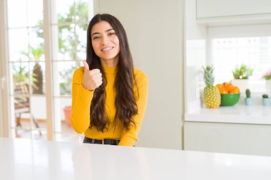 Genç güzel kadın evde beyaz masada hareketi el ile mutlu Yaşasın yapıyor. Başarı gösteren kameraya bakarak ifade onaylama.