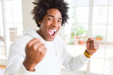 Afrika kökenli Amerikalı adam silah ile başarı için heyecanlı kazak giyen zafer kutluyor gülümseyen kaldırdı. Kazanan kavramı.