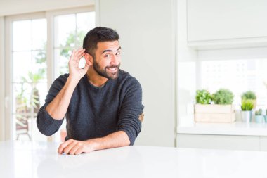 Evde rahat kazak giyen İspanyol yakışıklı bir işitme söylenti ya da dedikodu için dinleme kulak üzerinde el ile gülümseyen. Sağırlık kavramı.