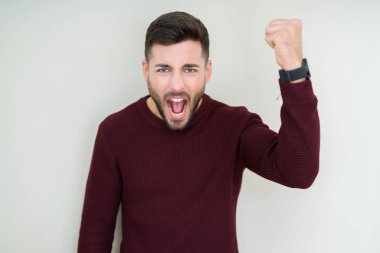 Genç yakışıklı adam kızgın ve kızgın hayal kırıklığı ve öfke ile bağırarak süre öfkeli yumruk yükselterek izole arka plan üzerinde bir kazak giyiyor. Öfke ve agresif kavramı.