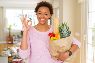 Kağıt çanta dolusu taze yiyecek parmak, mükemmel sembolü ile ok işareti yapıyor tutan genç Afro-Amerikan kadın