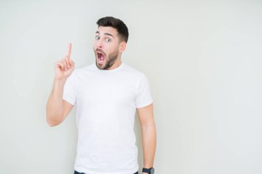 Başarılı fikirle izole arka plan üzerinde işaret parmağı rahat beyaz t-shirt giyen genç yakışıklı adam. Çıktıktan ve mutlu. Bir numara.