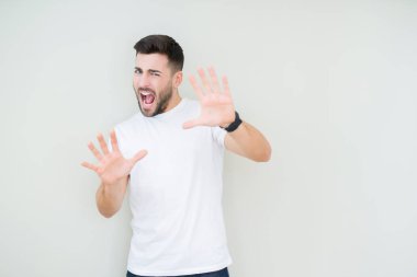 Şokta bağırarak korkuyor ve dehşet korku ifade dur hareketi el ile ile izole arka plan üzerinde rahat beyaz t-shirt giyen genç yakışıklı adam. Panik kavramı.