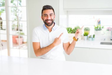Yakışıklı İspanyol erkek ev gülümseyen ve iki elleri ve parmakları ile tarafına işaret kamera bakarak casual beyaz t-shirt.