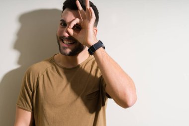 Yakışıklı delikanlı ile mutlu yüz el parmaklarının arasından seyir göz üzerinde ok işaretiyle yapıyor gülümseyen izole arka plan üzerinde