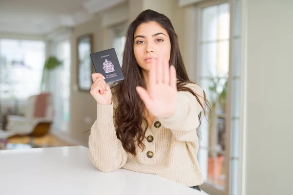 Young woman holding passport of Canada with open hand doing stop sign with serious and confident expression, defense gesture