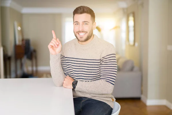 Young handsome man wearing a sweater at home with a big smile on face, pointing with hand and finger to the side looking at the camera.