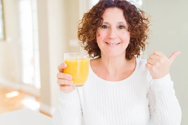 高级妇人滴着一杯新鲜的橙汁 用大拇指指着 带着幸福的脸向着身边展示 — 图库照片