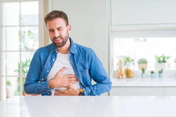 Handsome man at home with hand on stomach because indigestion, painful illness feeling unwell. Ache concept.