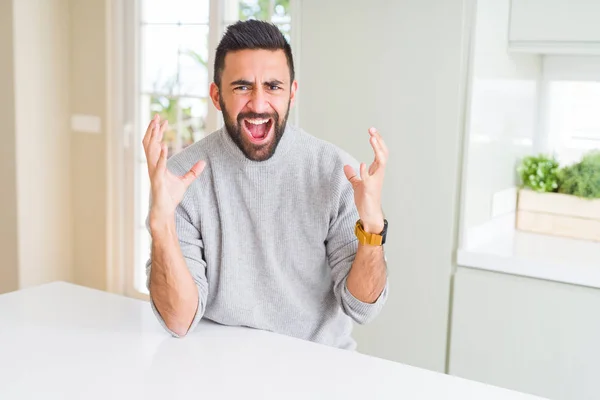 英俊的西班牙男子穿着休闲毛衣在家里疯狂和疯狂的大喊大叫 积极的表情和手臂抬起来 挫折的概念 — 图库照片