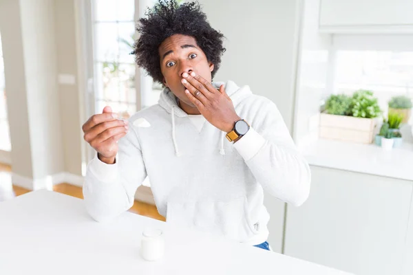 African American man eating healthy yogurt for breakfast cover mouth with hand shocked with shame for mistake, expression of fear, scared in silence, secret concept