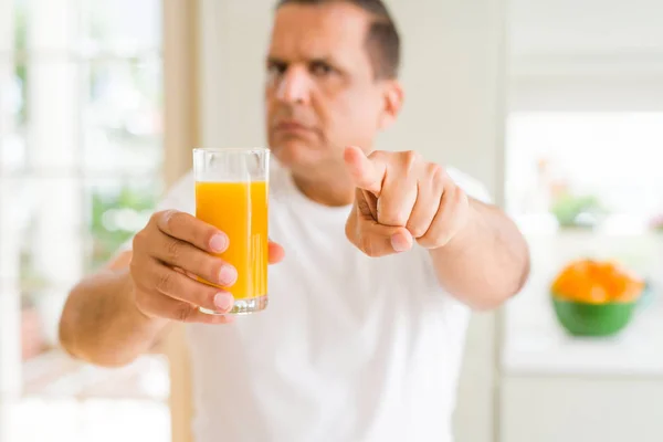 Średnim Wieku Człowiek Wypija Szklankę Soku Pomarańczowego Domu Wskazując Palcem — Zdjęcie stockowe