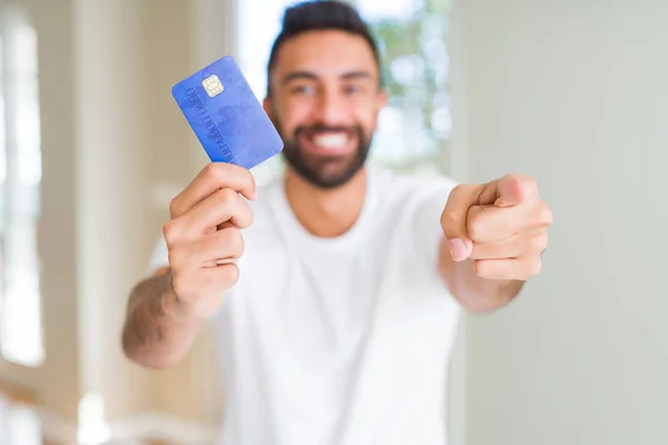 Handsome hispanic man holding credit card pointing with finger to the camera and to you, hand sign, positive and confident gesture from the front